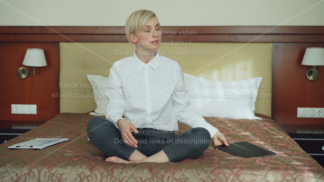 Smiling businesswoman put off laptop computer and taking yoga lotus position sitting relaxed on bed