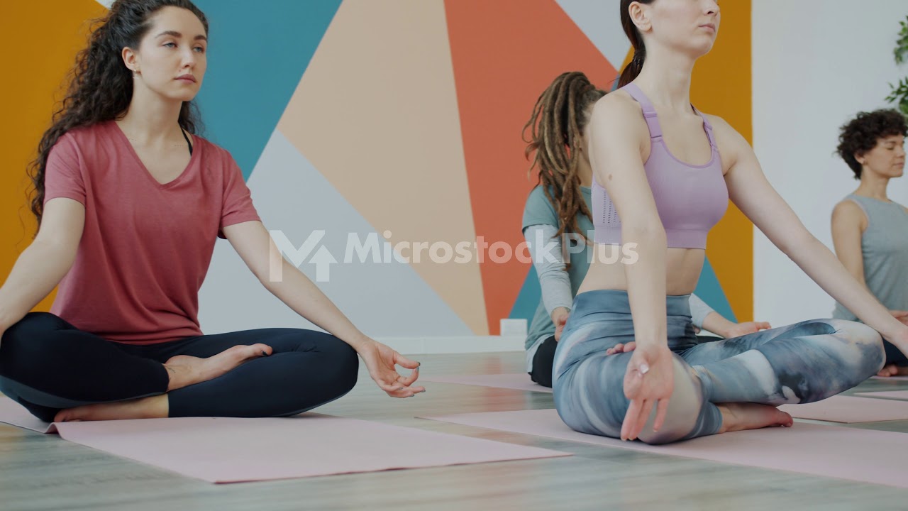 Group of young people meditating sitting in lotus position during yoga practice in studio
